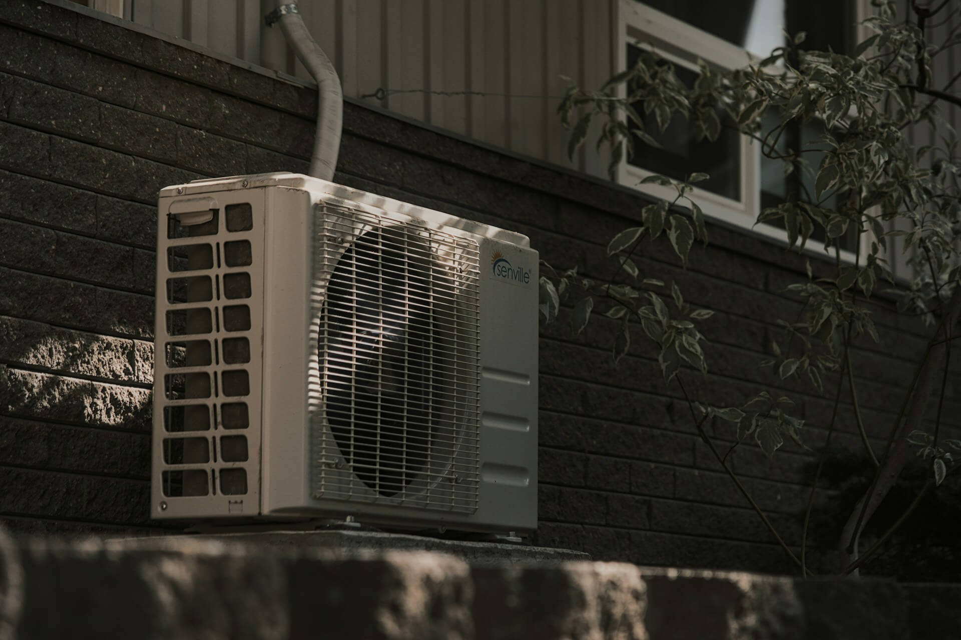 A white HVAC unit mounted on a brick wall. Image by Unsplash