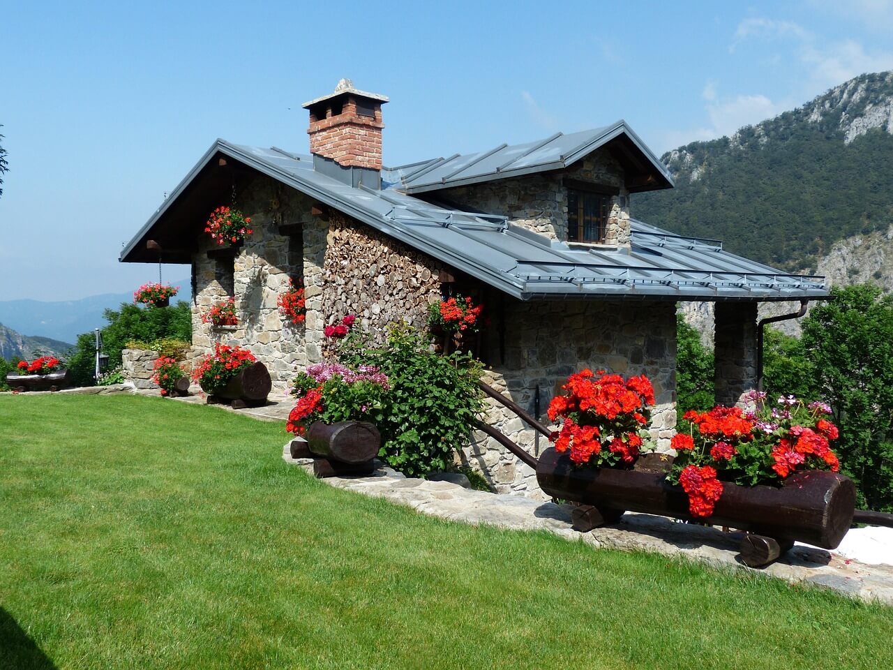 house with a green lawn, lots of flowers in pots. Image by Pixabay