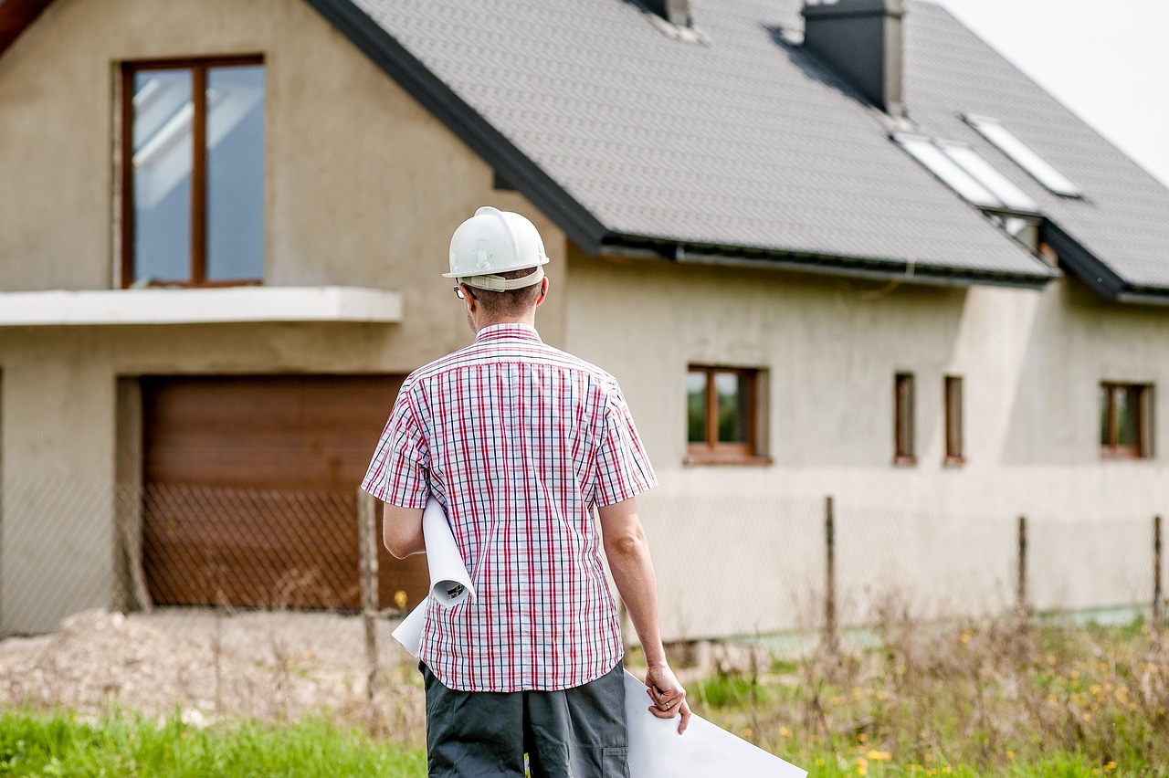 Architect with plans in his hands looking at a house. Image by Pixabay