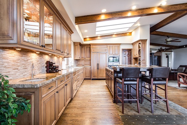 Large kitchen with wooden cabinets, island with chairs. Image by Pixabay