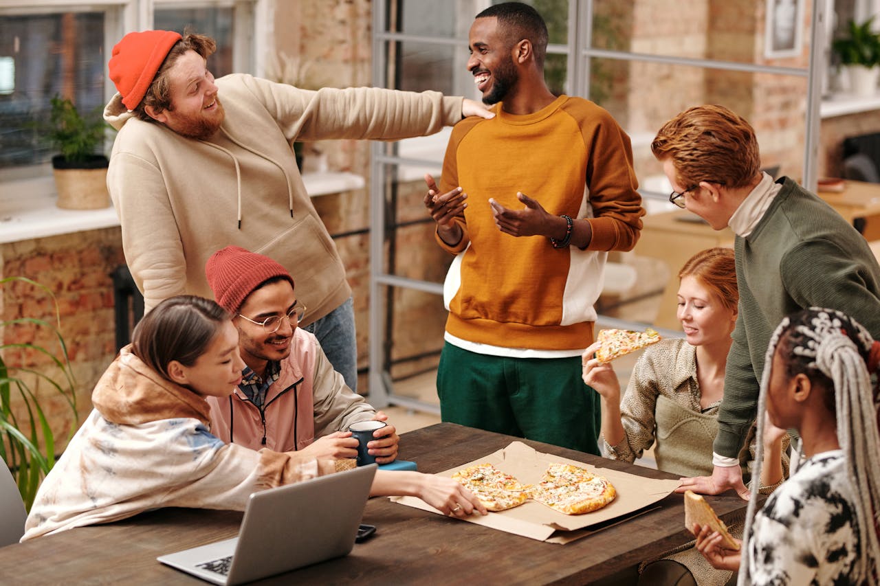 People sitting and standing around a table eating pizza. Image by Pexels