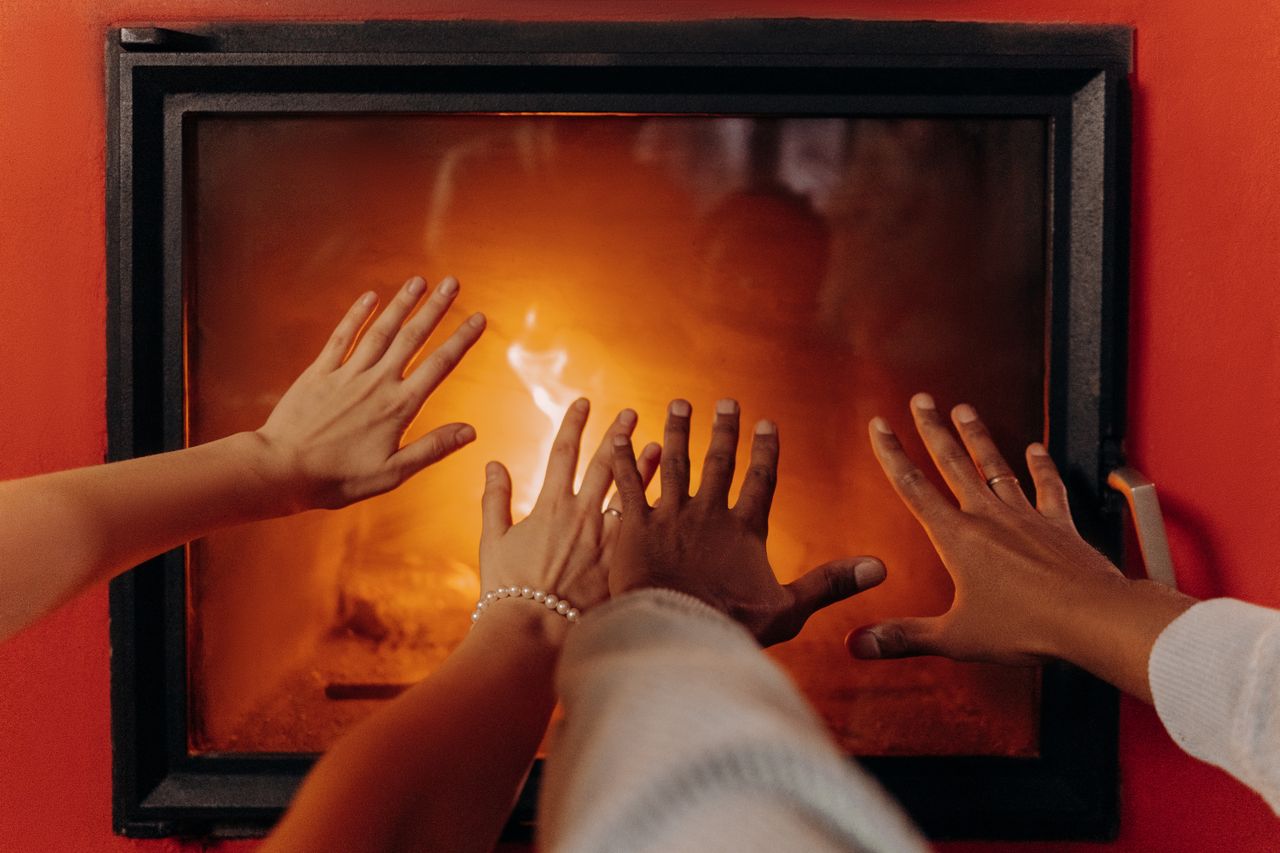 People heating their hands in front of a fireplace. Image by Pexels