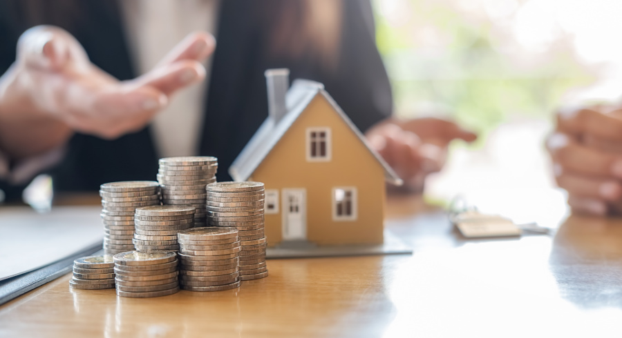 Coins, house on a table. Person in the background