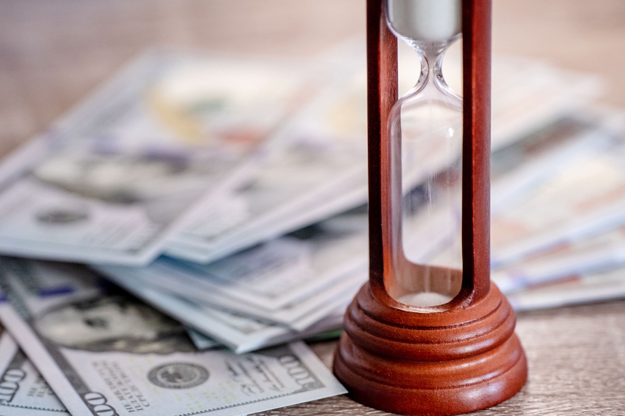 Money on a table, hour glass. Image by Pixabay