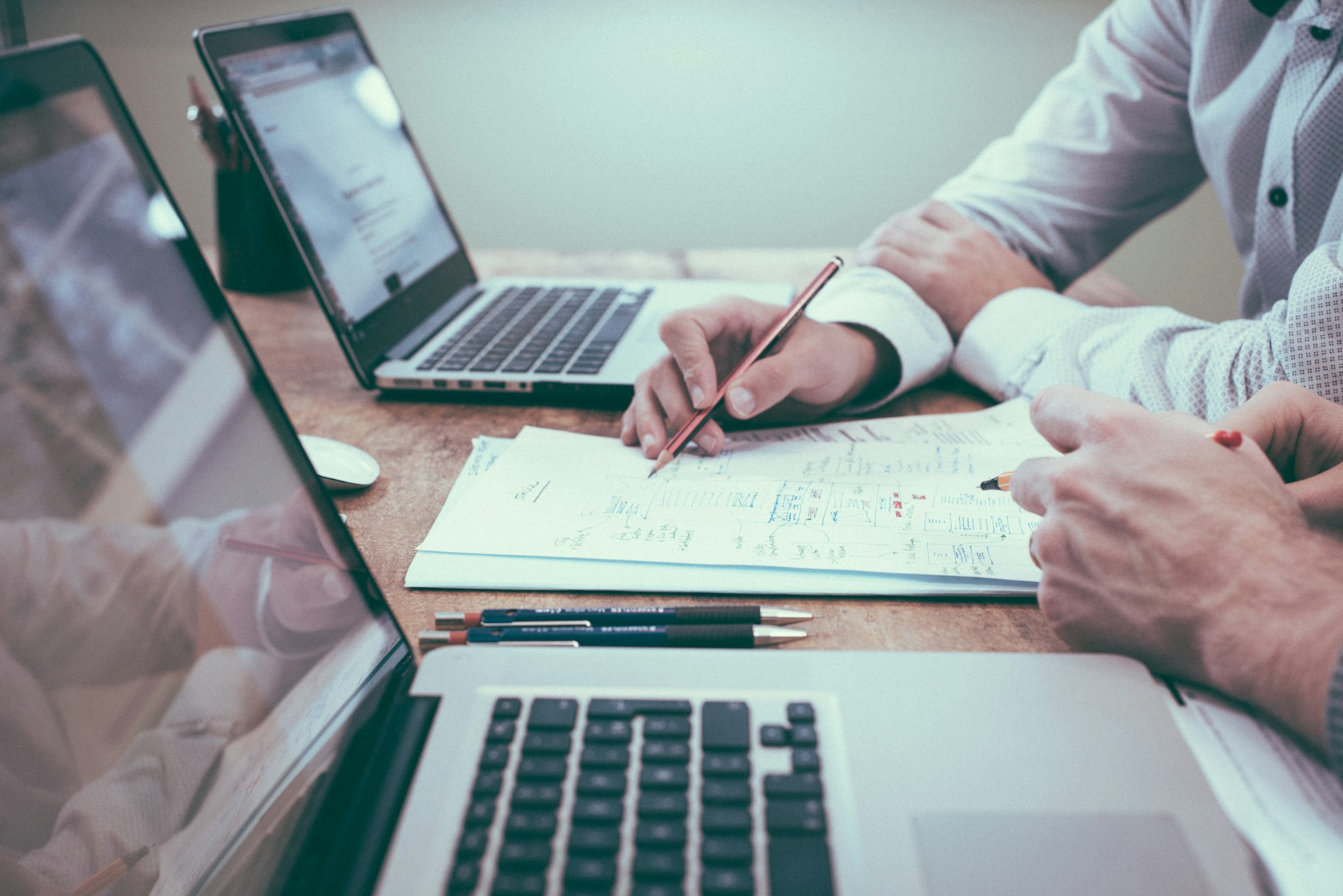 Person holding a pencil near a couple of laptops. Image by Unsplash