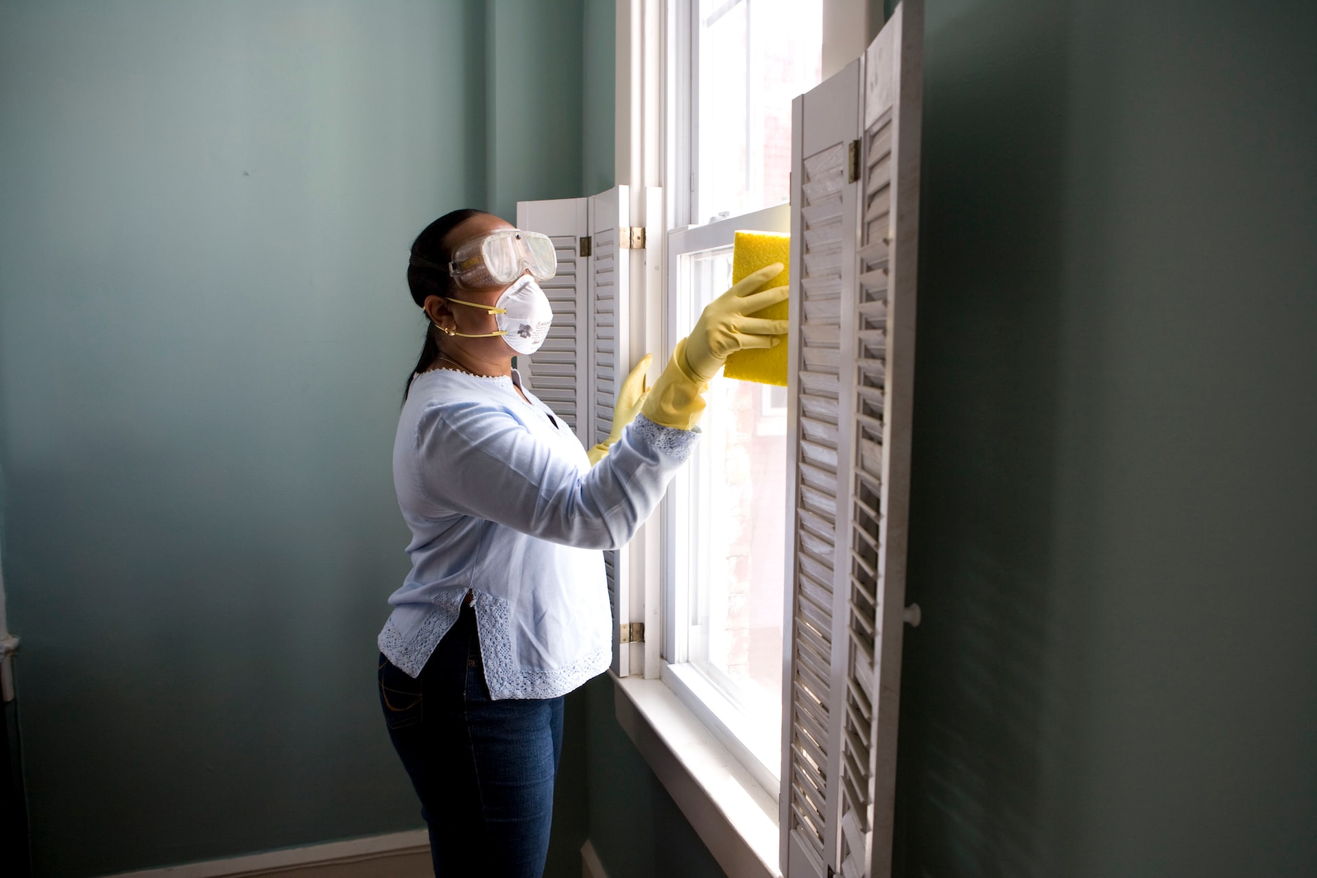person with a mask and googles cleaning a window. Image by Unsplash