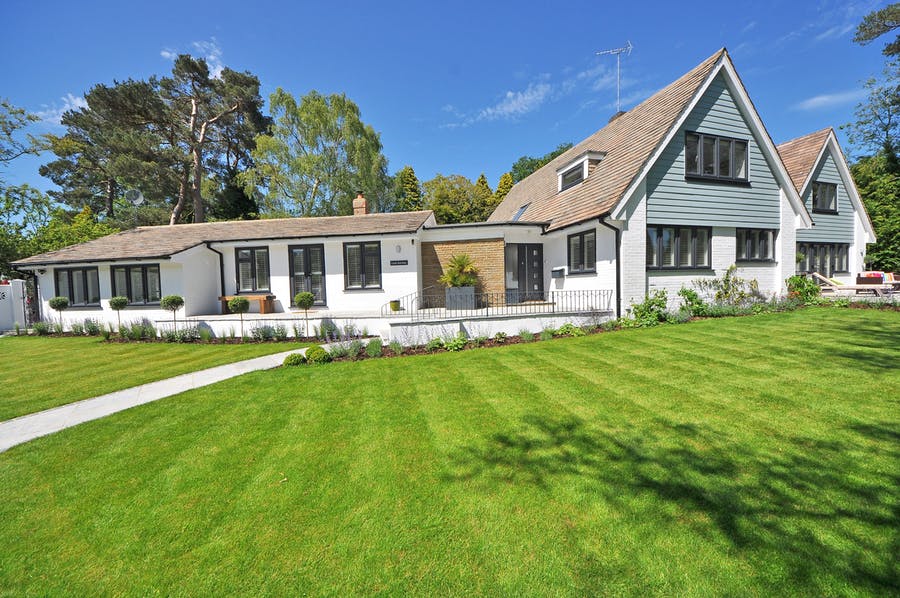 Large white and grey house with mature trees behind it and a wide grass lawn in front demonstrating well-maintained exterior landscaping