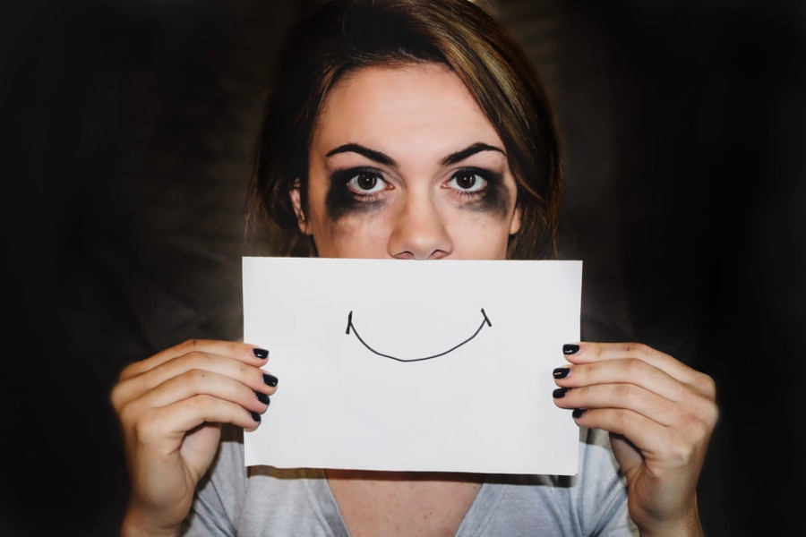 Person holding up a piece of paper with a drawn smiling mouth in front of her face